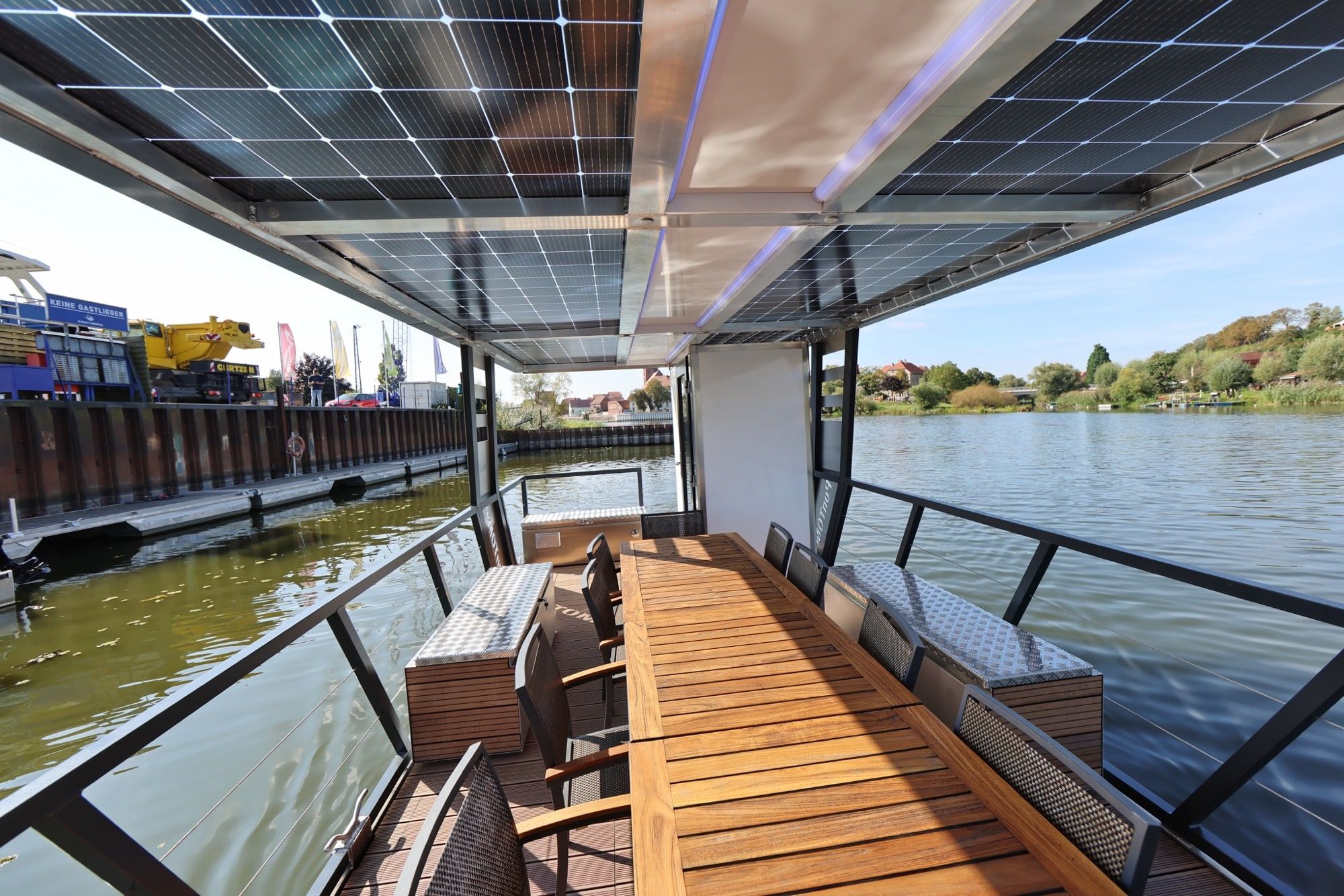 Überdachtes Hauptdeck des Solar-Charterboots PonTOM Empor 9.0 mit Holztisch, Sitzbänken und Blick auf die Havel
