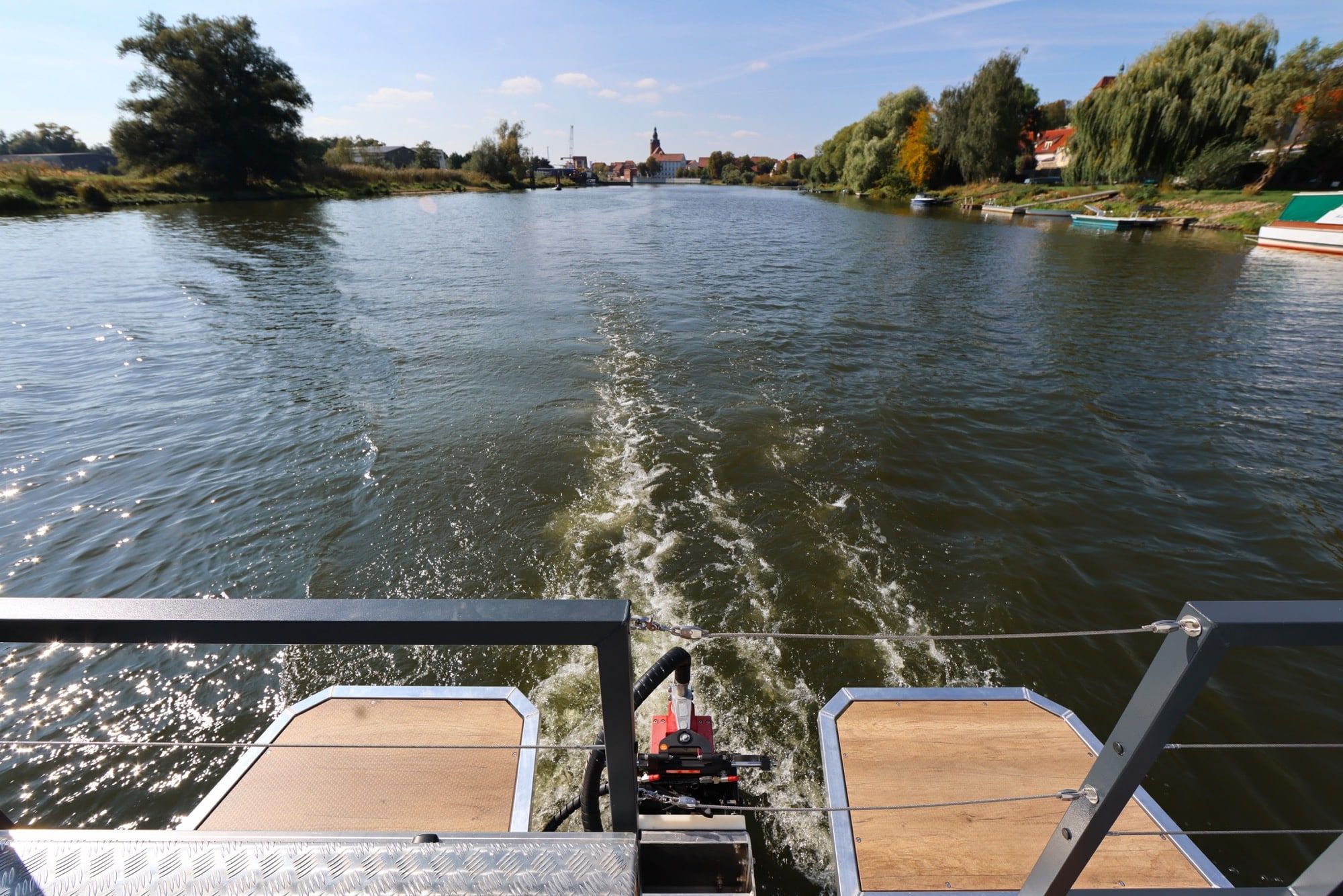Blick vom Heck des Charterboots PonTOM Empor 9.0 über das Kielwasser auf Havelberg und die Havellandschaft