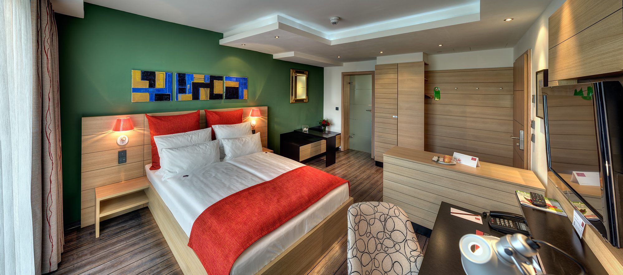 Superior-Zimmer im ArtHotel Kiebitzberg mit Doppelbett vor grüner Wand, roter Tagesdecke, moderner Kunst und Holzmöbeln