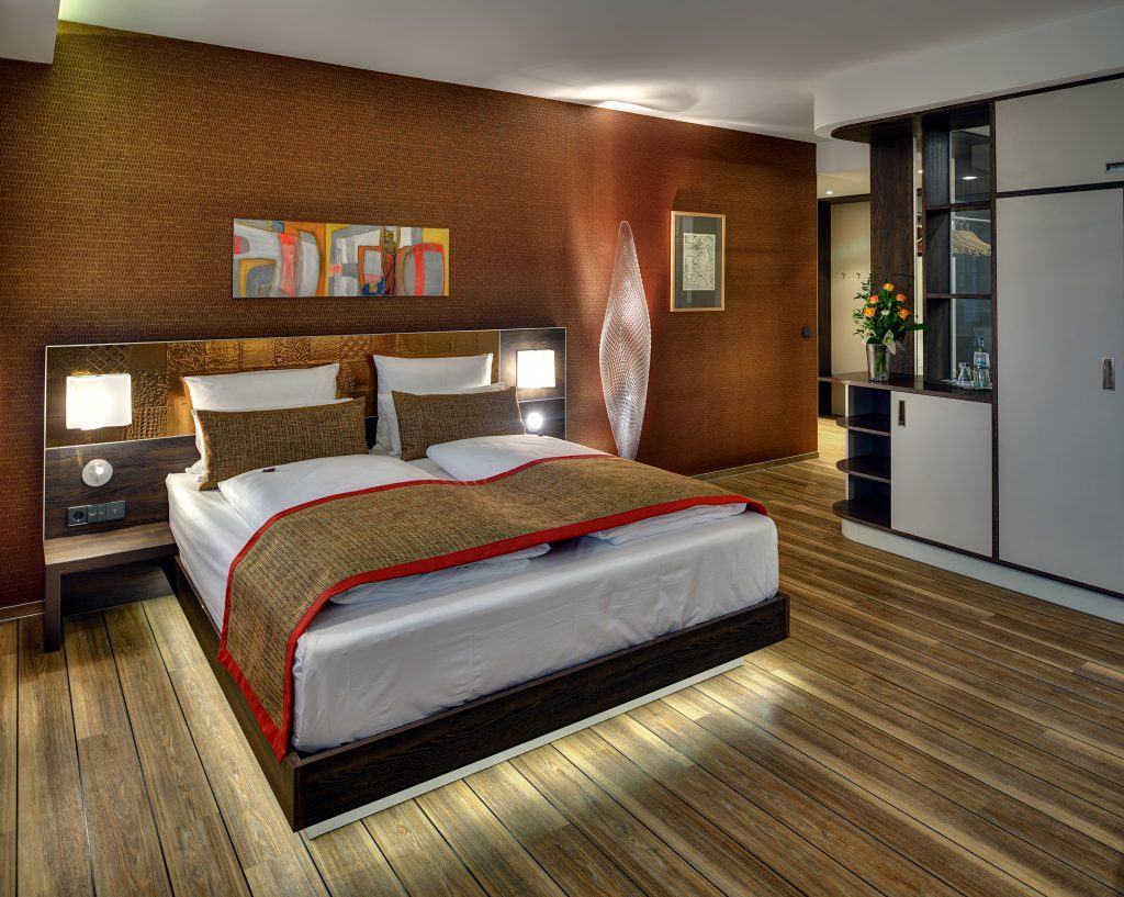 Wellness-Suite im ArtHotel Kiebitzberg mit Doppelbett vor terrakottafarbener Wand, Designerleuchte und Holzboden
